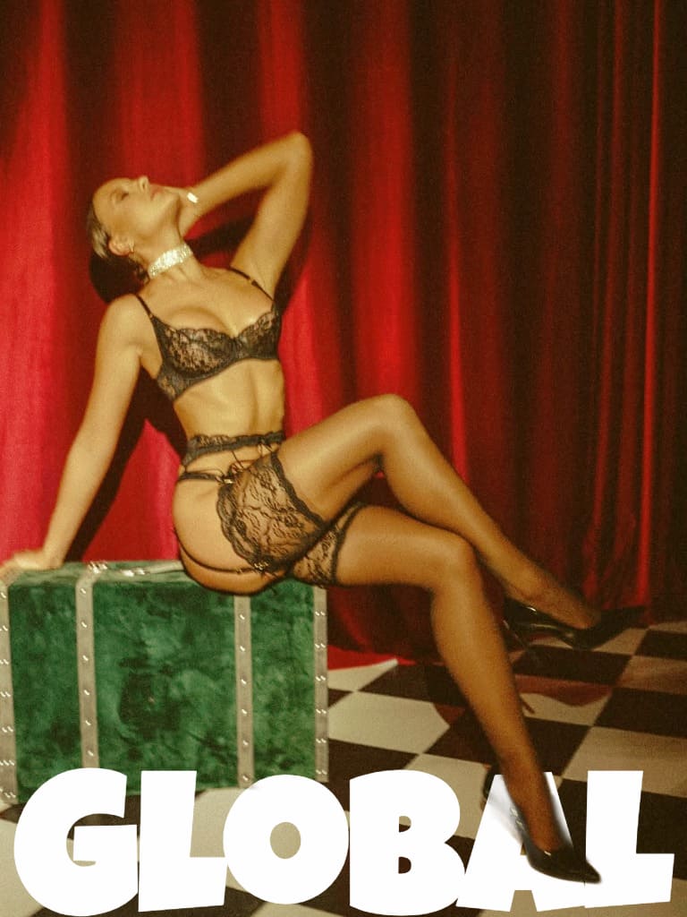 Luxury escort model in transparent lingerie posing by red curtain.
