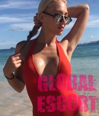 sexy escort blonde posing on the beach in a bright red swimsuit and black glasses